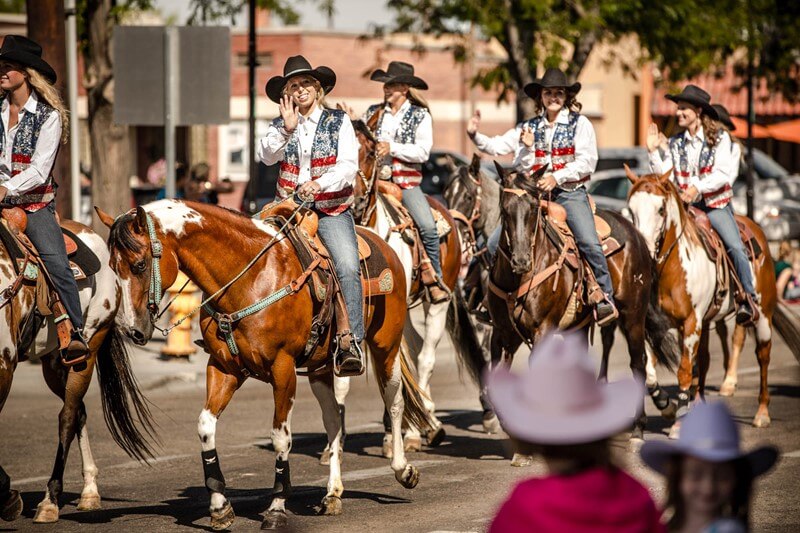 Cowgirls in sequined USA vests ride horses in a parade.